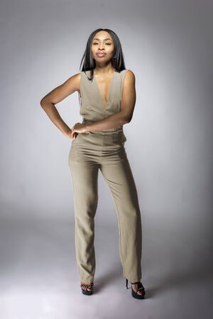 Beautiful black African American fashion model posing with humus grey or khaki clothing in a studio for fall collection catalog.  She is confidently showing the sleeveless top and matching pants.の写真素材