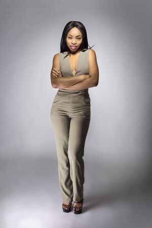 Beautiful black African American fashion model posing with humus grey or khaki clothing in a studio for fall collection catalog.  She is confidently showing the sleeveless top and matching pants.の写真素材