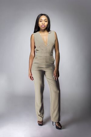 Beautiful black African American fashion model posing with humus grey or khaki clothing in a studio for fall collection catalog.  She is confidently showing the sleeveless top and matching pants.の写真素材