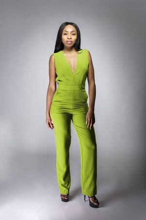 African American fashion model posing with lime green v-neck jumpsuit in a studio for fall collection catalog.  She is confidently showing the sleeveless top and matching pants.の写真素材
