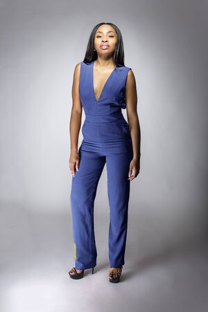 African American fashion model posing with royal or navy blue v-neck jumpsuit outfit in a studio for fall collection catalog.  She is confidently showing the sleeveless top and matching pants.の写真素材