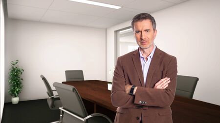 Middle-Aged businessman with gray hair and wearing a brown jacket standing in an office.  Depicts startup and corporate business.  He is looking upset or angry.の写真素材