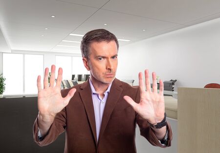 Middle-Aged businessman with gray hair and wearing a brown jacket standing in an office.  Depicts startup and corporate business.  He is holding hands up for stop gesture.の写真素材