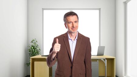 Middle-Aged businessman with gray hair and wearing a brown jacket standing in an office.  Depicts startup and corporate business.  He is holding thumbs up in approval.の写真素材