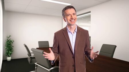 Middle-Aged businessman with gray hair and wearing a brown jacket standing in an office.  Depicts startup and corporate business.  He is smiling and happy.の写真素材