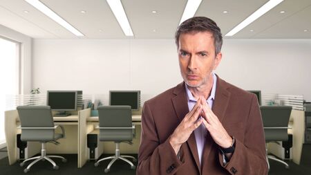 Middle-Aged businessman with gray hair and wearing a brown jacket standing in an office.  Depicts startup and corporate business.  He has a secret to tell.の写真素材
