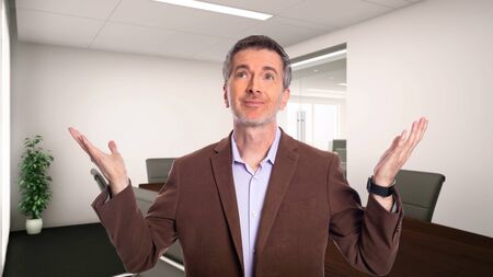 Middle-Aged businessman with gray hair and wearing a brown jacket standing in an office.  Depicts startup and corporate business.  He is advertising or presenting something.の写真素材