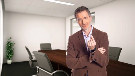 Middle-Aged businessman with gray hair and wearing a brown jacket standing in an office.  Depicts startup and corporate business.  He is doing a money gesture.の写真素材