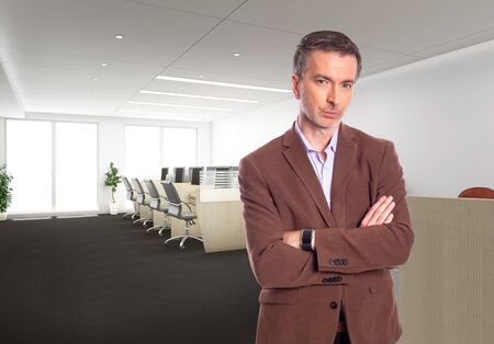 Middle-Aged businessman with gray hair and wearing a brown jacket standing in an office.  Depicts startup and corporate business.  He is looking confident or arrogant.の写真素材