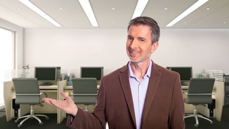 Middle-Aged businessman with gray hair and wearing a brown jacket standing in an office.  Depicts startup and corporate business.  He is advertising or presenting something.の写真素材