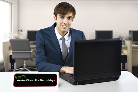 Businessman on a desk with a closed sign using a computer to type a vacation auto reply email.  He...