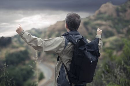Middle-aged Caucasian male hiker trekking alone in the mountains. The overcast sky is peaceful and...