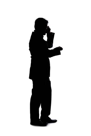 Full body silhouette of a businessman isolated on a white background. He is using a cell phone or mobile device to talk or send messages.の写真素材