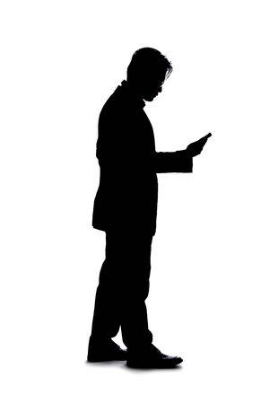 Full body silhouette of a businessman isolated on a white background. He is using a cell phone or mobile device to talk or send messages.の写真素材