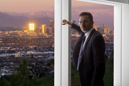 Businessman wearing a suit looking at the buildings of downtown Los Angeles from an office window.  The man looks like a politician like a mayor, or an architect or a real estate developer working in LA.の写真素材