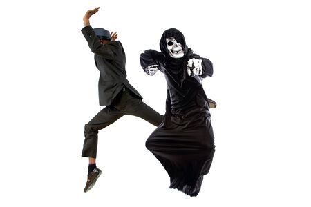 Man in a grim reaper halloween ghost costume having fun and scaring a grown businessman in a suit.  The image depicts pranks and being surprised.  Isolated on a white background.の写真素材