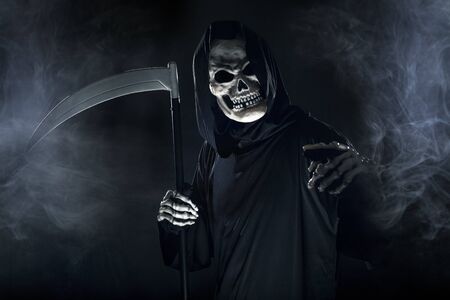 Scary looking grim reaper ghost wielding a scythe or sickle coming out of the fog.  The haunting monster depicts death and evil and is a common Halloween theme.の写真素材