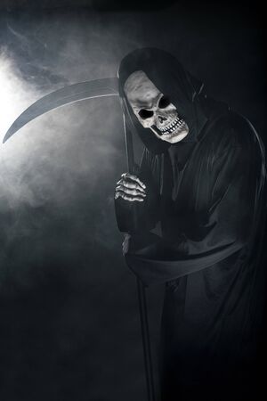 Scary looking grim reaper ghost wielding a scythe or sickle coming out of the fog.  The haunting monster depicts death and evil and is a common Halloween theme.の写真素材