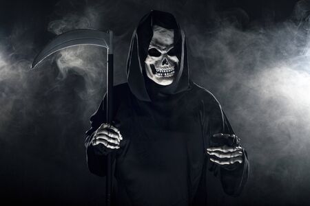 Scary looking grim reaper ghost wielding a scythe or sickle coming out of the fog.  The haunting monster depicts death and evil and is a common Halloween theme.の写真素材