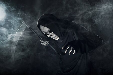 Scary looking grim reaper ghost wielding a scythe or sickle coming out of the fog.  The haunting monster depicts death and evil and is a common Halloween theme.の写真素材