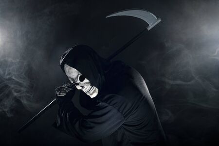 Scary looking grim reaper ghost wielding a scythe or sickle coming out of the fog.  The haunting monster depicts death and evil and is a common Halloween theme.の写真素材