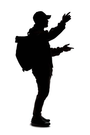 Silhouette of a man wearing a backpack looking like a traveler or hiker trekking.  He is gesturing like he is talking or speakingの写真素材