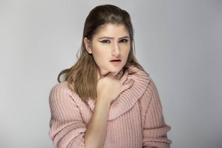 Close up portrait of a young Caucasian woman wearing a pink sweater on a grey background.  The model looks sick with a sore throatの写真素材