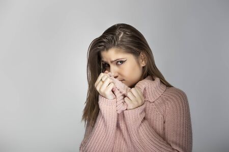 Close up portrait of a young Caucasian woman wearing a pink sweater on a grey background.  The model looks scared or terrifiedの写真素材