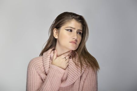 Close up portrait of a young Caucasian woman wearing a pink sweater on a grey background.  The model looks sick with a sore throatの写真素材