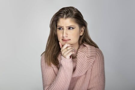 Close up portrait of a young Caucasian woman wearing a pink sweater on a grey background.  The model looks stressed out and worriedの写真素材