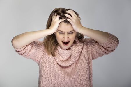 Close up portrait of a young Caucasian woman wearing a pink sweater on a grey background. She looks angry and in stressの写真素材