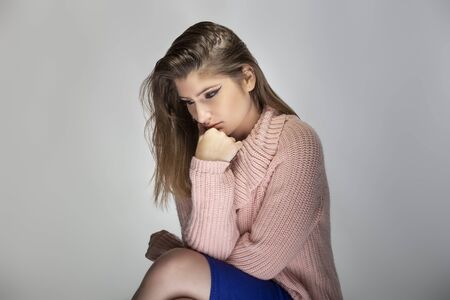 Close up portrait of a young Caucasian woman wearing a pink sweater on a grey background.  She looks sad and depressedの写真素材