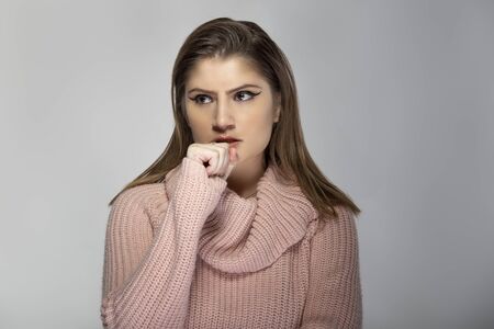 Close up portrait of a young Caucasian woman wearing a pink sweater on a grey background. She looks angry and in stressの写真素材