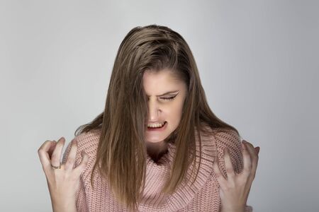 Close up portrait of a young Caucasian woman wearing a pink sweater on a grey background. She looks angry and in stressの写真素材