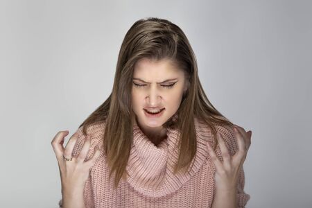 Close up portrait of a young Caucasian woman wearing a pink sweater on a grey background. She looks angry and in stressの写真素材