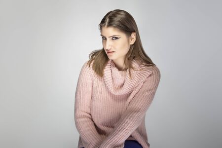 Close up portrait of a young Caucasian woman wearing a pink sweater on a grey background.  She looks disgusted or repulsed by somethingの写真素材