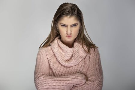 Close up portrait of a young Caucasian woman wearing a pink sweater on a grey background. She looks angry and in stressの写真素材