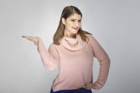 Close up portrait of a young Caucasian woman wearing a pink sweater on a grey background.  She is presenting something like and advertisementの写真素材