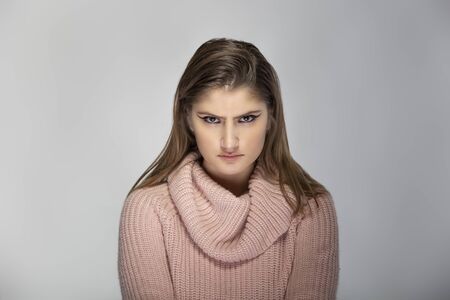 Close up portrait of a young Caucasian woman wearing a pink sweater on a grey background. She looks angry and in stressの写真素材