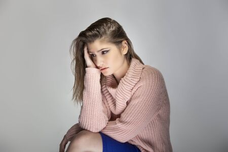 Close up portrait of a young Caucasian woman wearing a pink sweater on a grey background.  She looks sad and depressedの写真素材