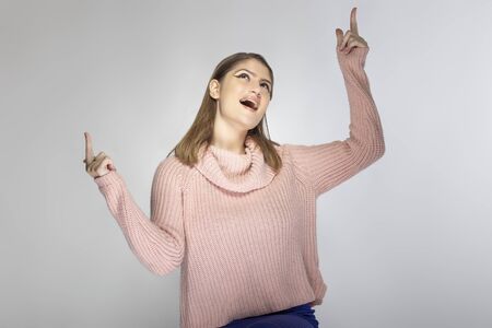Close up portrait of a young Caucasian woman wearing a pink sweater on a grey background.  She is presenting something like and advertisementの写真素材