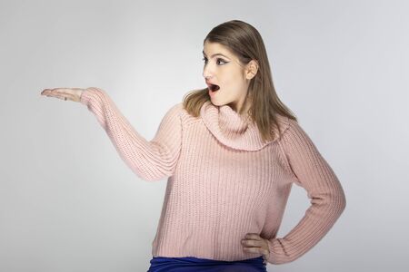 Close up portrait of a young Caucasian woman wearing a pink sweater on a grey background.  She is presenting something like and advertisementの写真素材