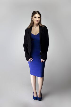 Fashion model wearing a blue dress and a black formal jacket posing as a confident businesswoman in a outfit.  Shot in a studio in catalog styleの写真素材