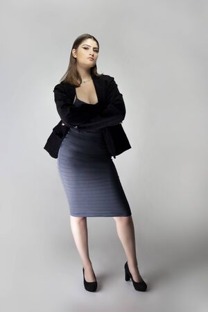 Female model posing as a sexy business woman looking confident like a boss or a manager. Her outfit is a trendy charcoal blue dress with a business suit or jacket. の写真素材