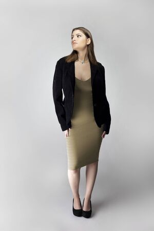 Female model posing as a sexy business woman looking confident like a boss or a manager. Her outfit is a trendy brown or tan dress with a business suit or jacket. の写真素材