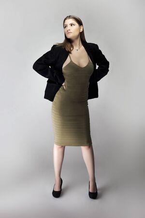 Female model posing as a sexy business woman looking confident like a boss or a manager. Her outfit is a trendy brown or tan dress with a business suit or jacket. の写真素材