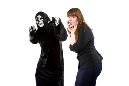 Scared businesswoman paranoid of catching a deadly disease represented by the grim reaper.  She is frightened of contracting a pandemic illness such as coronavirusの写真素材
