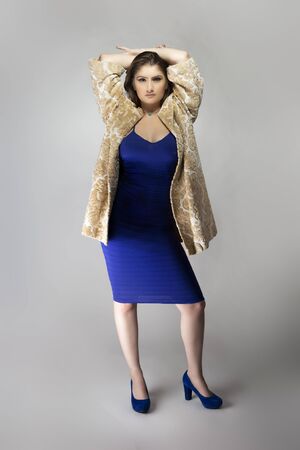 Female fashion model wearing a beige brocade wool or cotton coat and a blue sexy dress in studio catalog style.  Depicts spring or fall trendsの写真素材