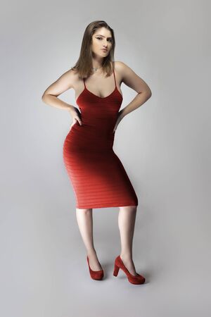 Catalog style studio shot of a Caucasian female fashion model wearing a wine or rose red summer dress.  She is posing to show trendy style of the outfit or clothingの写真素材