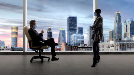 Businessman and businesswoman working in the office during a pandemic and keeping social distance and wearing protective face masks to prevent viral infection of covidの写真素材